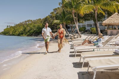 Man and woman walking along beach hand in hand, while guests relax on loungers