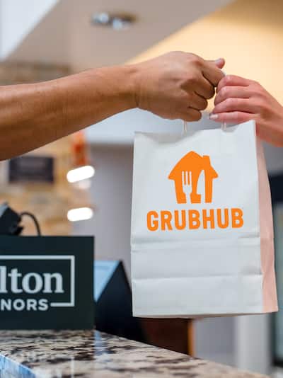 A person's hand passing a bag with the Grub Hub logo to another person