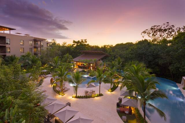 Vista ao pôr do sol do exterior do hotel e da área da piscina com palmeiras